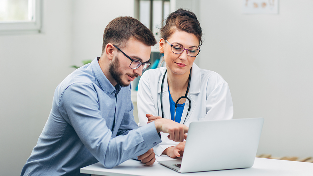 Ein junger Patient zeigt einer Ärztin etwas auf einem Laptop.